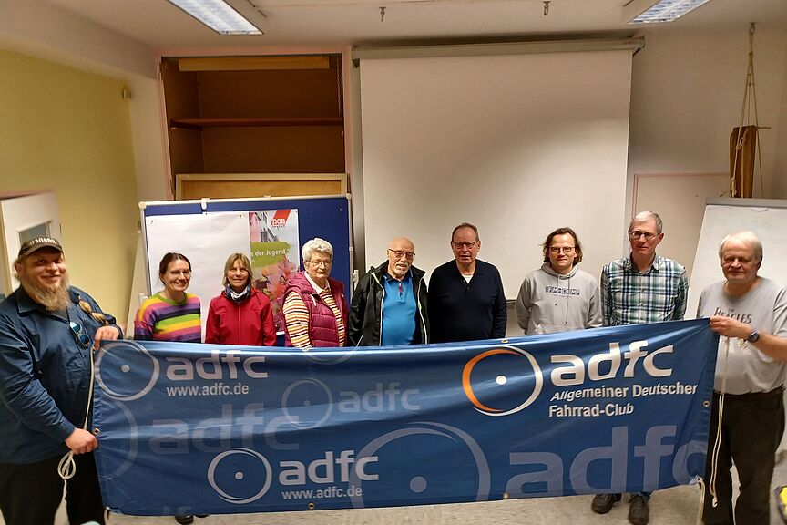 MV 2024 In einem Raum halten 2 Menschen ein blaues Banner, dahinter stehen Menschen