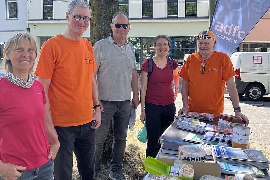 Neben einem Infotisch mit Broschüren stehen 5 Personen in sommerlicher Kleidung